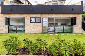 Una casa moderna de dos pisos con amplios ventanales y puertas de vidrio, fachada de piedra y un césped bien cuidado.