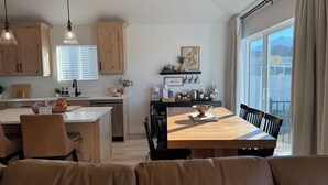 A modern kitchen with wooden cabinets, a dining area with a wooden table and chairs, and a large window offering a view of the outdoors. - Cozy Winter Escape, New Build with 3 Car Garage (Tooele)