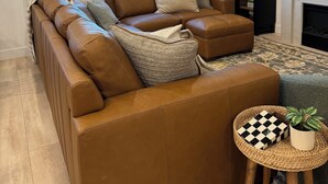 A modern living room with a large sectional sofa, a flat-screen TV, a fireplace, and a view of a distant landscape. - Cozy Winter Escape, New Build with 3 Car Garage (Tooele)