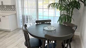 Ein Essbereich mit einem runden Tisch und Stühlen, einer Zimmerpflanze und Blick auf ein Schwimmbad durch große Fenster.
