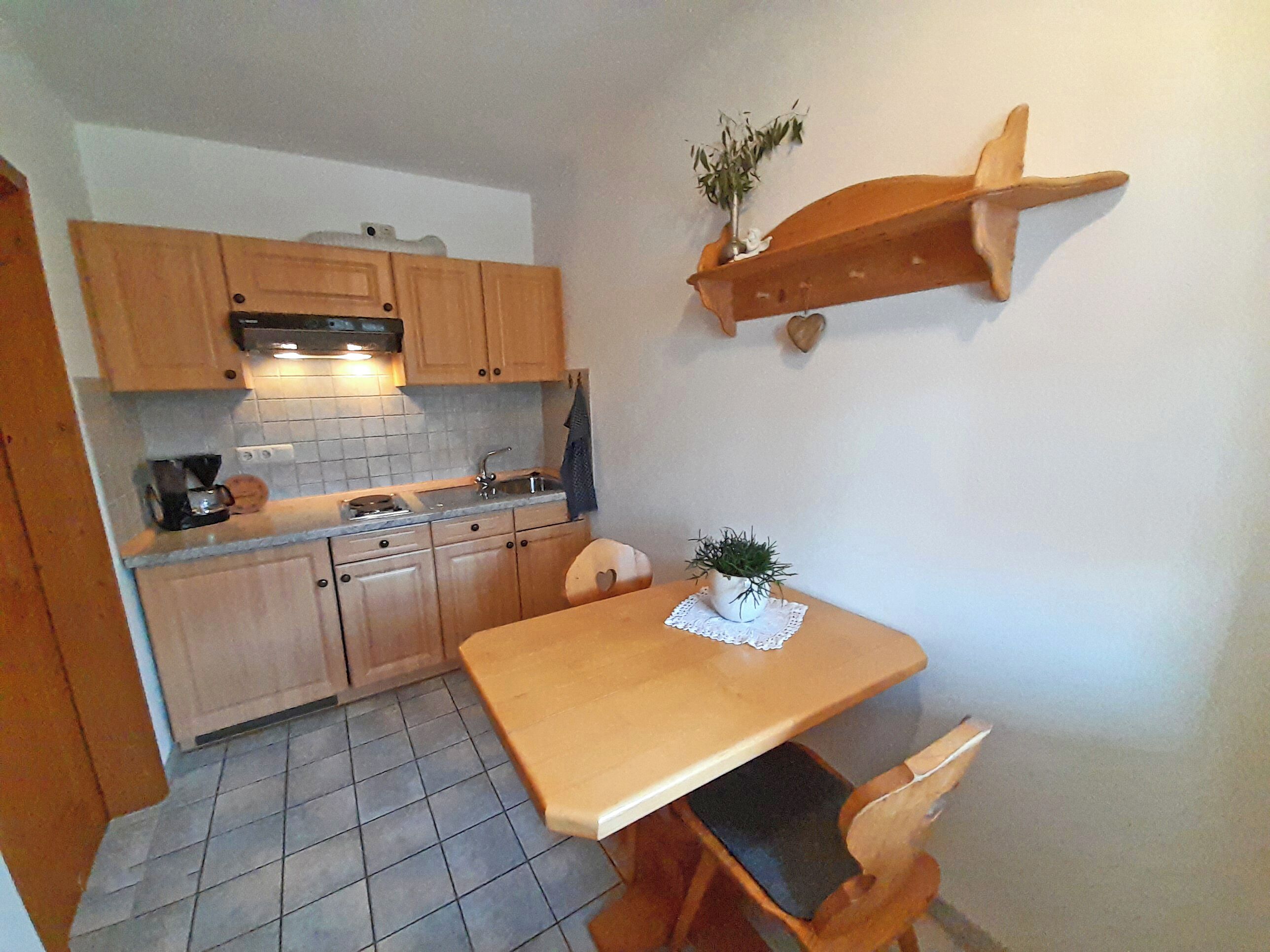 Een kleine keuken met houten kastjes, een spoelbak en een eettafeltje met stoelen.