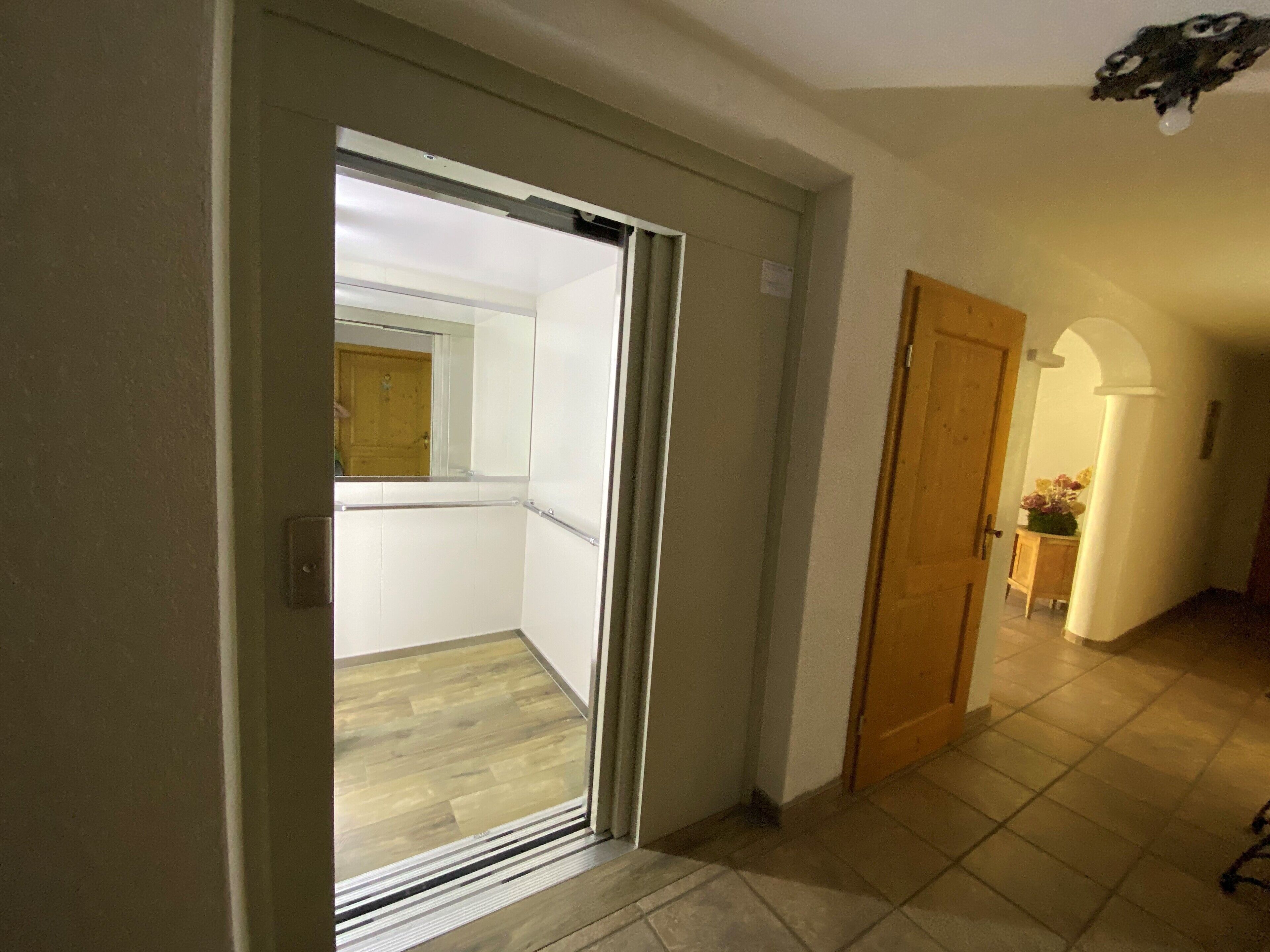 A hallway with a sliding glass door leading to a balcony, a wooden door, and a tiled floor.