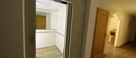 A hallway with a sliding glass door leading to a balcony, a wooden door, and a tiled floor.