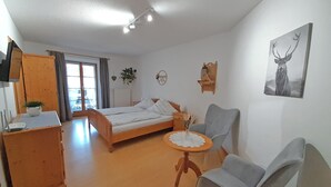 Un dormitorio con cama, escritorio, silla, mesita pequeña, planta y estante en la pared.