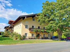 Ein zweistöckiges Gebäude mit gelber Fassade, mehreren Balkonen und einem Baum davor.