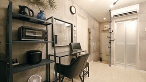 A modern kitchen with a microwave, kettle, and fan. There is a laptop on a desk and a chair. The room has wooden flooring and a clock on the wall. - AirHOMETOKYO EBISU 101 (Tokyo)