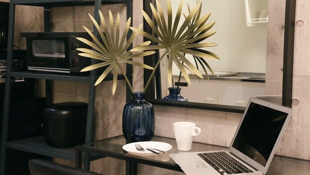 A modern kitchen with a microwave, a laptop on a glass table, a white mug, and two decorative plants in a blue vase. - AirHOMETOKYO EBISU 101 (Tokyo)