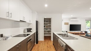 A modern kitchen with white cabinetry, a built-in oven, and a dishwasher. There is a wooden floor and a dining area with a TV and a sign that says "Life is better at the beach." - Fireside Retreat in Cowes (Cowes)