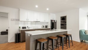 A modern kitchen with white cabinets, a central island with stools, a black refrigerator, and a coffee machine. - Fireside Retreat in Cowes (Cowes)