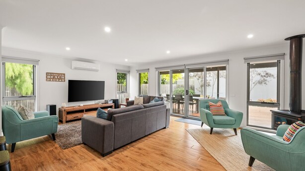 A spacious living room with a grey sofa, teal armchairs, a flat-screen TV, and a fireplace. - Fireside Retreat in Cowes (Cowes)