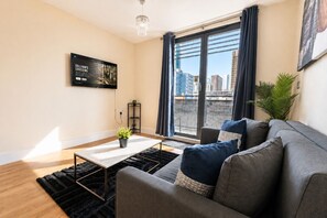 Una sala de estar moderna con un sofá, una mesa de centro, un televisor y un ventanal con vistas a la ciudad.