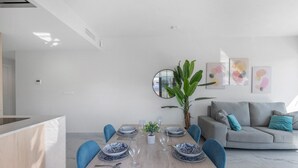 Een moderne eetruimte met een houten tafel voor vier personen, blauwe stoelen en een grijze bank met turquoise kussens.