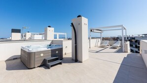 Een terras op het dak met een jacuzzi, een pergola met lounge stoelen en een helder uitzicht op de skyline van de stad.