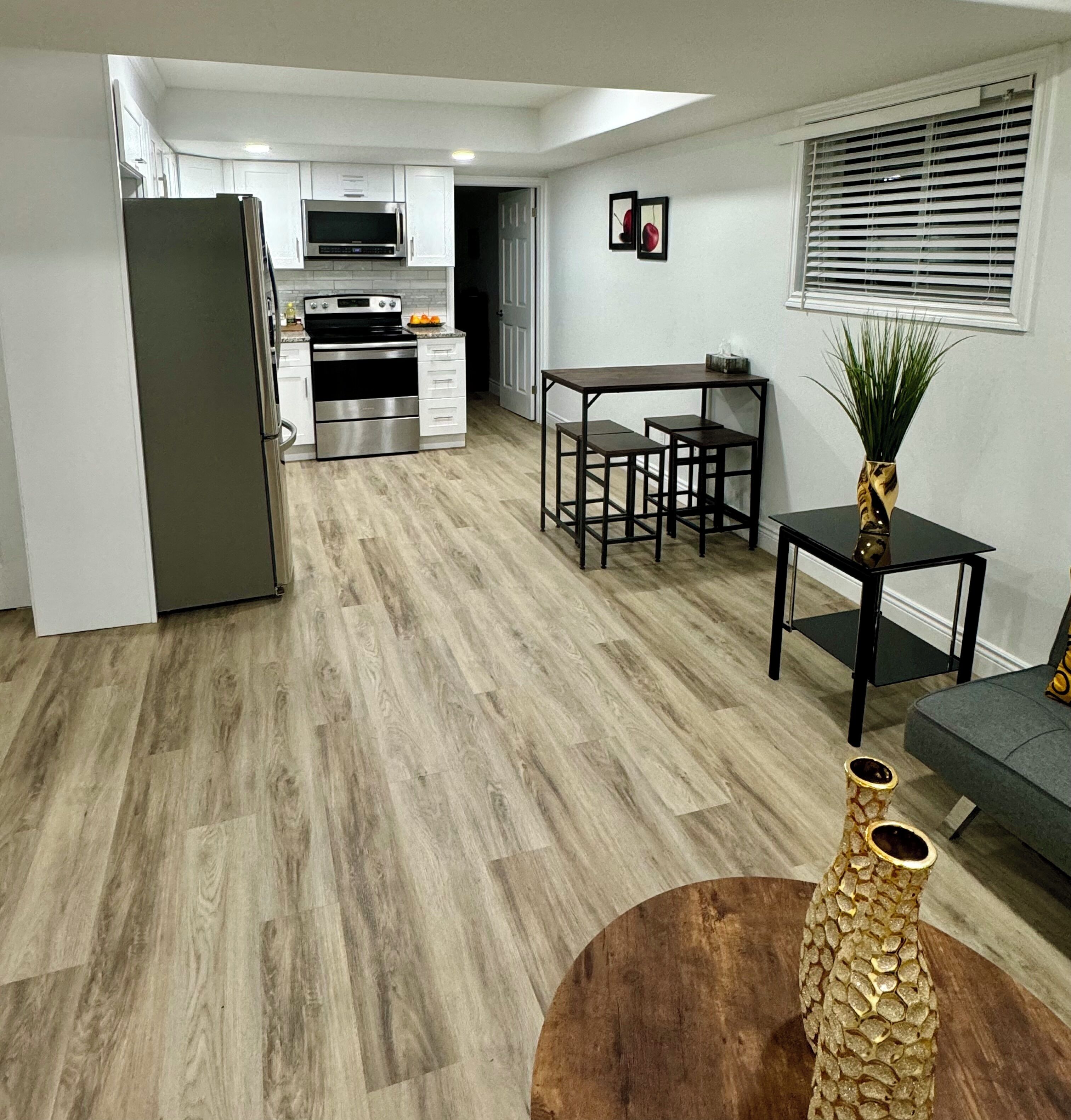 Eine moderne Küche mit Kühlschrank, Mikrowelle und Backofen, ein Essbereich mit Tisch und Stühlen sowie eine Wohnbereich mit Sofa und dekorativer Vase.