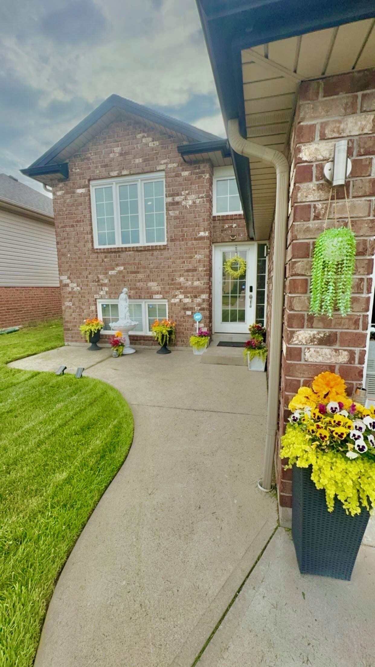 A two-story brick house with a front porch, a white door, and a small garden area with flowers and a statue.