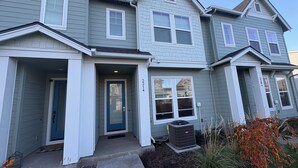 A two-story house with a front porch, a blue door, and a small front yard with a tree and a flower bed. - Haven at Reeds Crossing - Quiet 3-bedroom townhome with AC in charming Hillsboro (Hillsboro)