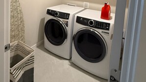 A laundry room with two front-loading washing machines, wooden cabinets above, a red bottle, and a laundry basket. - Haven at Reeds Crossing - Quiet 3-bedroom townhome with AC in charming Hillsboro (Hillsboro)