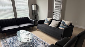 A modern living room with a black sofa, a glass coffee table, and a patterned rug. - Haven at Reeds Crossing - Quiet 3-bedroom townhome with AC in charming Hillsboro (Hillsboro)