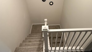 Eine Teppichstufen-Treppe mit weißen Geländern und drei schwarzen, runden Leuchten an der Wand.
