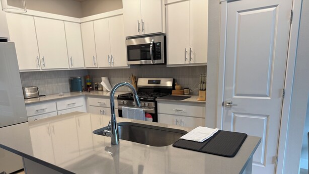 A modern kitchen with white cabinets, stainless steel appliances, and a central island with a sink and a black mat. - Haven at Reeds Crossing - Quiet 3-bedroom townhome with AC in charming Hillsboro (Hillsboro)