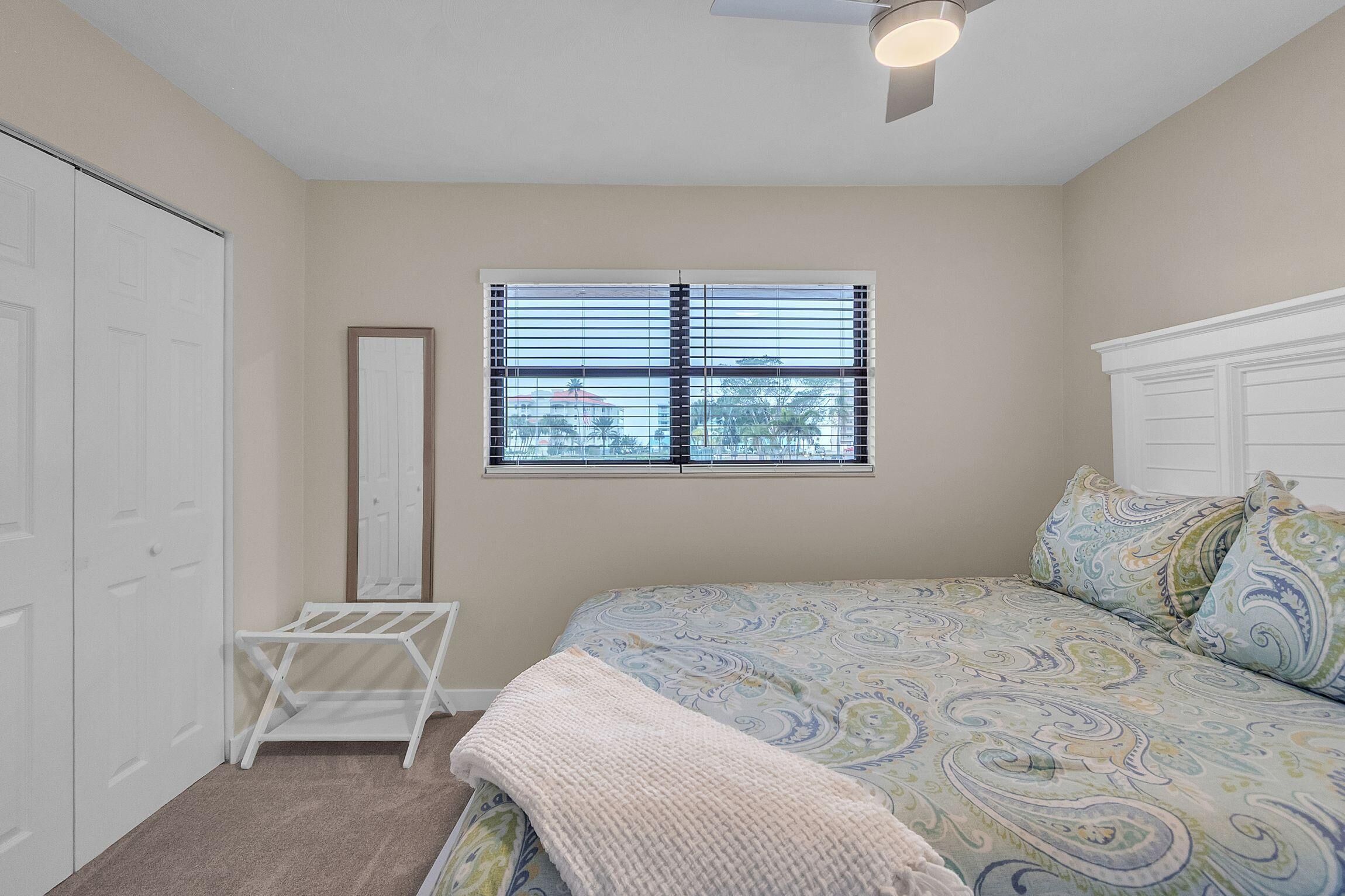 A bedroom with a bed, a window with blinds, a ceiling fan, and a white wardrobe.