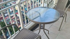 Un balcon doté d’une table ronde en verre et de deux fauteuils en osier, donnant sur une zone urbaine densément construite.