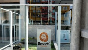 Een modern gebouw met een glazen gevel, een bord met een logo, en een woongebouw op de achtergrond.