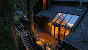 Ein modernes Haus mit einem Glasbalkon, einer Holzterrasse und einer Treppe, die zum oberen Stockwerk führt.