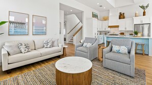 Ein modernes Wohnzimmer mit einer Couch, Sesseln, einem Couchtisch und einer Küchenzeile inklusive Schränken und Kühlschrank.