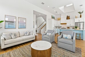 A modern living room with a sofa, armchairs, a coffee table, and a kitchen area with cabinets and a refrigerator. - Luxury Palmilla home w/ gas grill & views - pool, gym, beach, & golf access (Port Aransas)