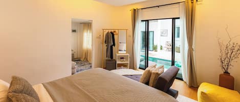 Habitación de hotel con cama, zona de estar, una mesita y vista a la piscina.