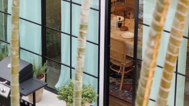 Ett modernt hus med stora glasfönster, en uteplats med grill och krukväxter.