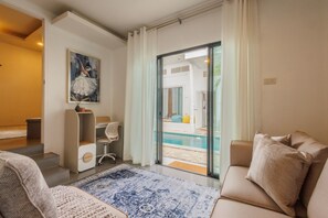 Ein modernes Wohnzimmer mit einem beigefarbenen Sofa, einem gemusterten Teppich, einem Bild an der Wand und einer Glastür zum Poolbereich.