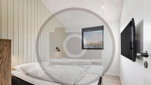 A modern bedroom with a bed, a mounted TV, and a window with a view of trees. - Amazing home in Hemmet with sauna (Hemmet)