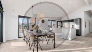A modern kitchen with a central island, a dining area with a round table and chairs, and large windows offering a view of the outdoors. - Amazing home in Hemmet with sauna (Hemmet)