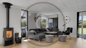 A modern living room with a fireplace, grey sofa, ottoman, and a large window offering a view of the outdoors. - Stunning home in Hemmet with sauna (Hemmet)