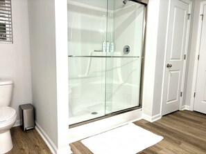 Een moderne badkamer met een douchecabine van glas, een toilet, een prullenbak en een witte vloerkleden.