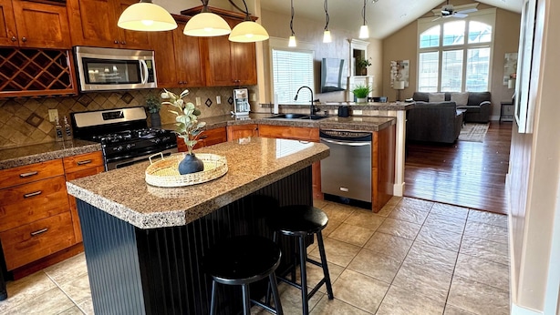 A spacious kitchen with granite countertops, wooden cabinets, and a central island with bar stools. - Baldwin Retreat | Spacious Stay w/ 3 King Beds (Meridian)