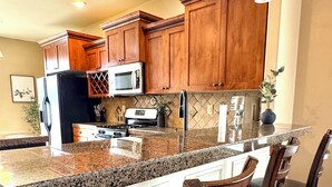 A kitchen with wooden cabinets, granite countertops, and a central island with bar stools. - Baldwin Retreat | Spacious Stay w/ 3 King Beds (Meridian)
