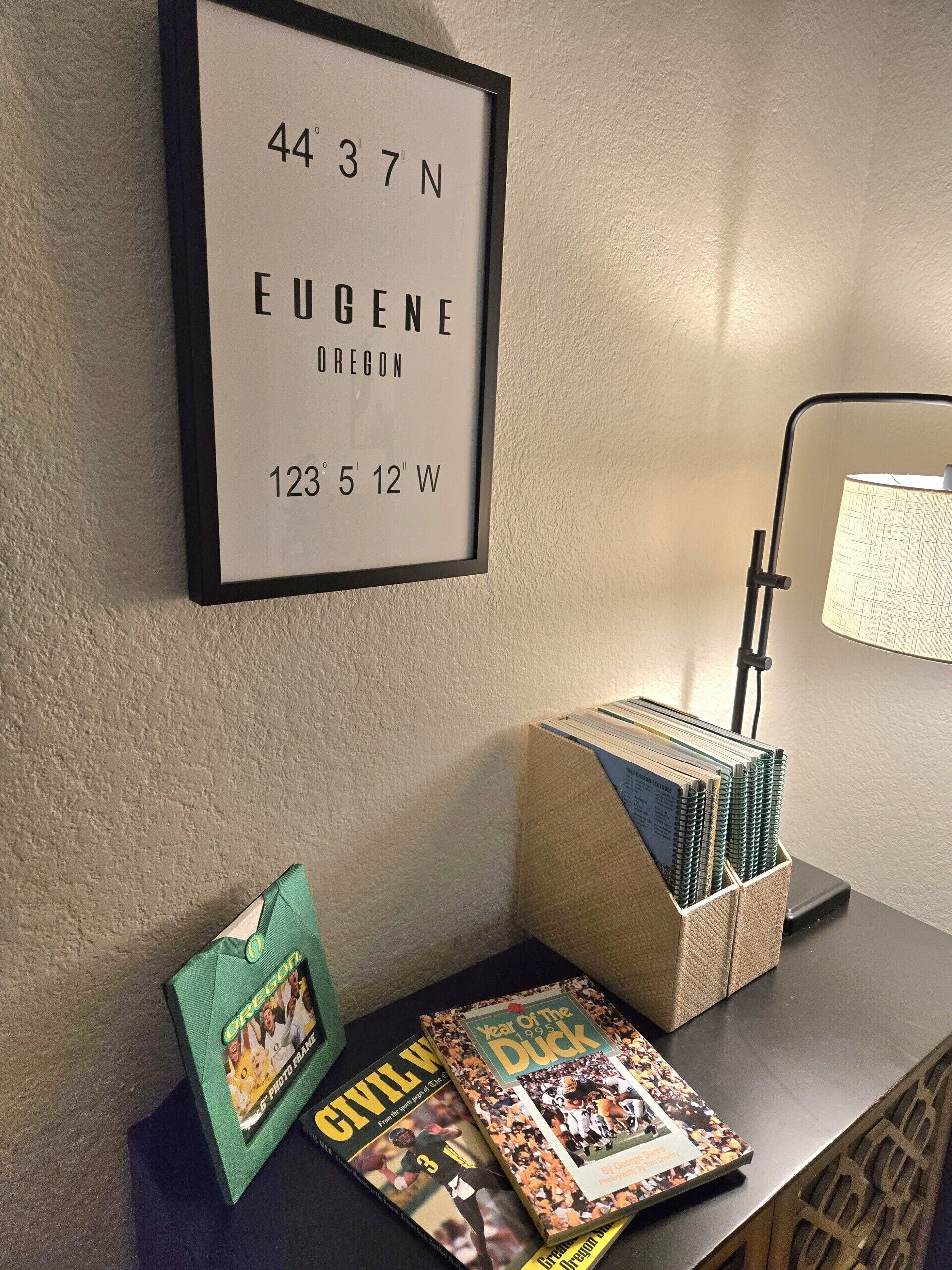 Une carte encadrée avec des coordonnées, un bureau avec une lampe, une pile de cahiers à spirales et deux livres intitulés « Guerre de Sécession » et « L’année du canard ».