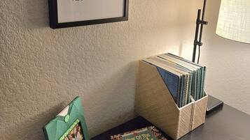 A framed map with coordinates, a desk with a lamp, a stack of spiral notebooks, and two books titled 'Civil War' and 'Year of the Duck'.