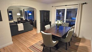 Ein modernes Wohnzimmer mit Essbereich, Holzboden und einem großen Fenster mit Vorhängen.