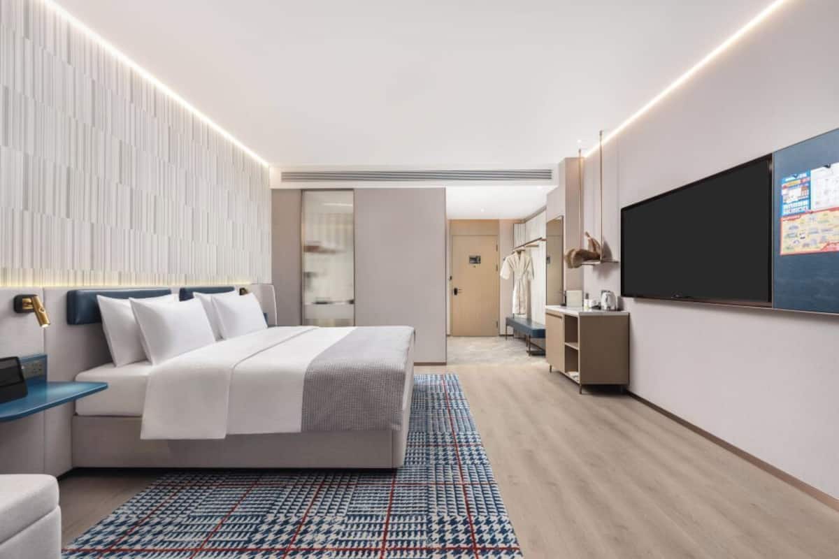 Una camera d'albergo moderna con un letto, un comodino, una TV e un tappeto decorato.