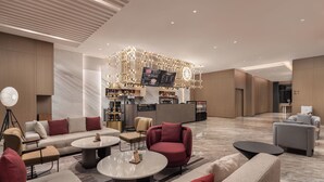 Een moderne hotellobby met een bar, zitgedeeltes en een kroonluchter.