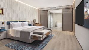 Een moderne slaapkamer met een bed, nachtkastjes, een bank, een spiegel en een schuifdeur naar een badkamer.