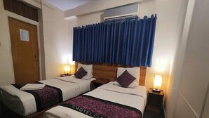 Ένα δωμάτιο ξενοδοχείου με δύο κρεβάτια, ένα ξύλινο προσκέφαλο, ένα παράθυρο με μπλε κουρτίνες, φωτιστικά κομοδίνου και μια πόρτα με μια ανακοίνωση.