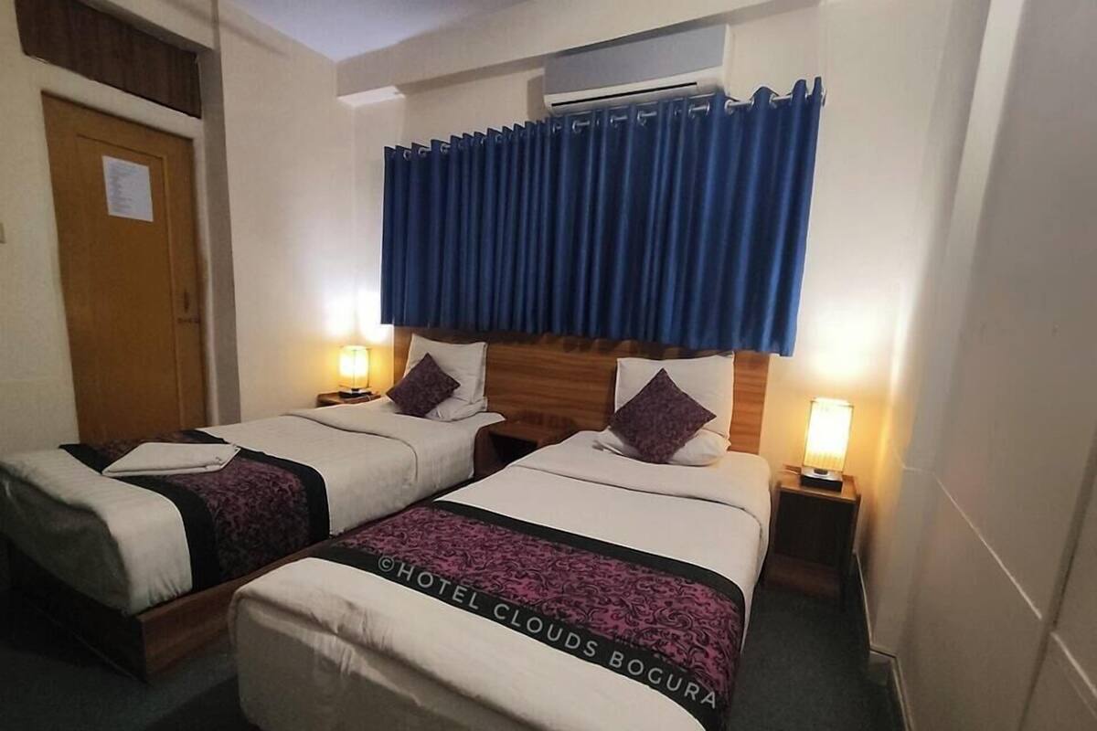 Een hotelkamer met twee bedden, een houten hoofdbord, een raam met blauwe gordijnen, bedlampen en een deur met een bericht.