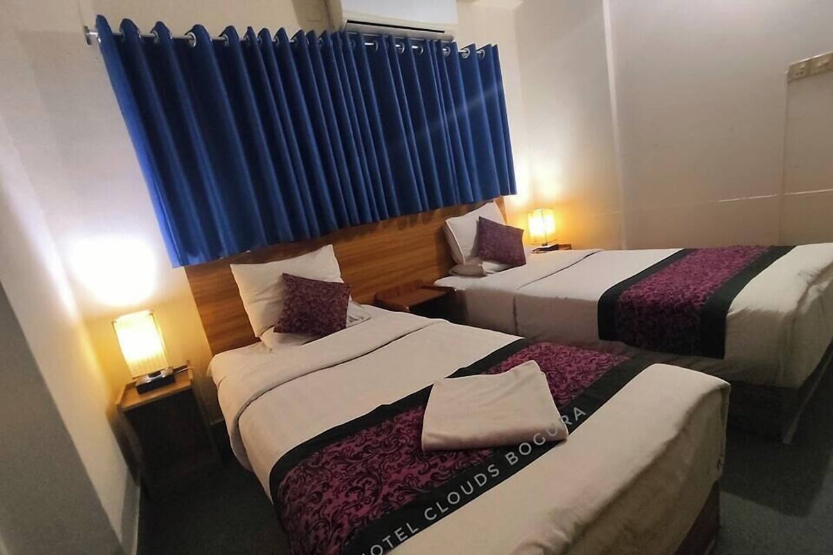 Een hotelkamer met twee bedden, een blauw gordijn, bedlampjes en een houten hoofdeinde.