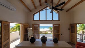 A room with a large window overlooking a beach, wooden ceiling beams, and three black vases on a table. - Beach Hose with Private Pool. Casa Quinta Nayaa (El Tomatal)