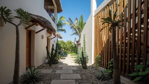 A narrow pathway with stepping stones leading to a wooden gate, surrounded by various plants and a clear blue sky. - Beach Hose with Private Pool. Casa Quinta Nayaa (El Tomatal)